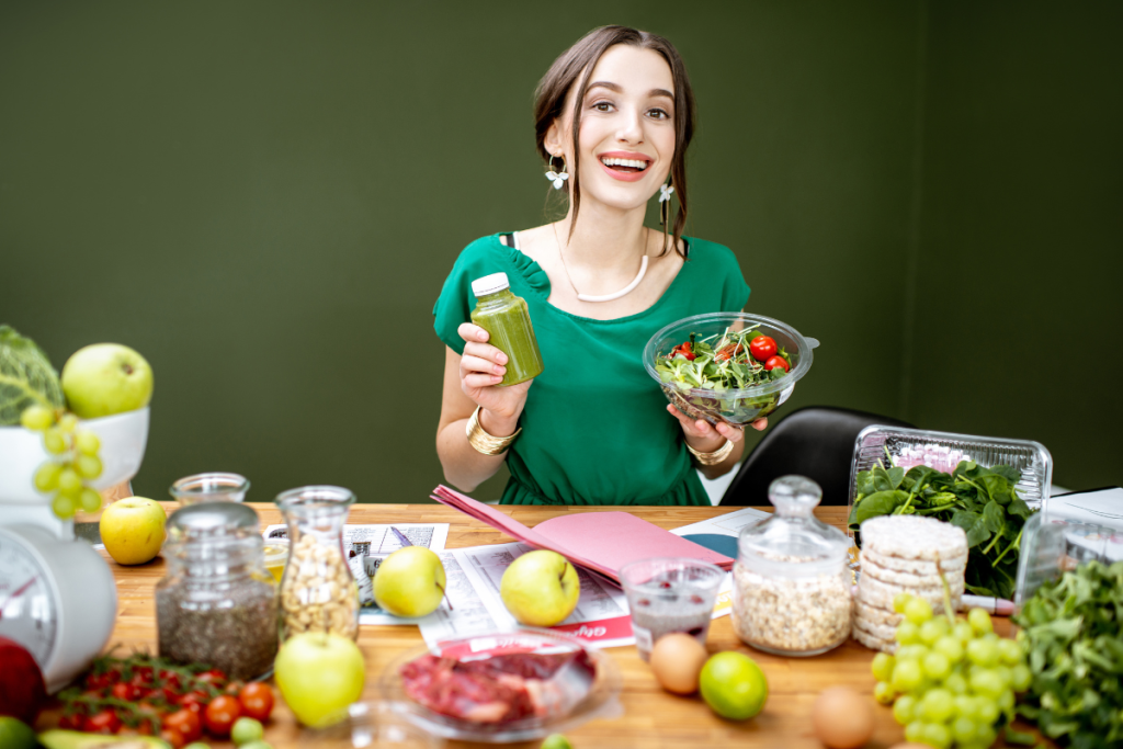 Portrait of a beautiful woman as a dietitian sitting with smoothie, salad and various healthy food ingredients in the green office