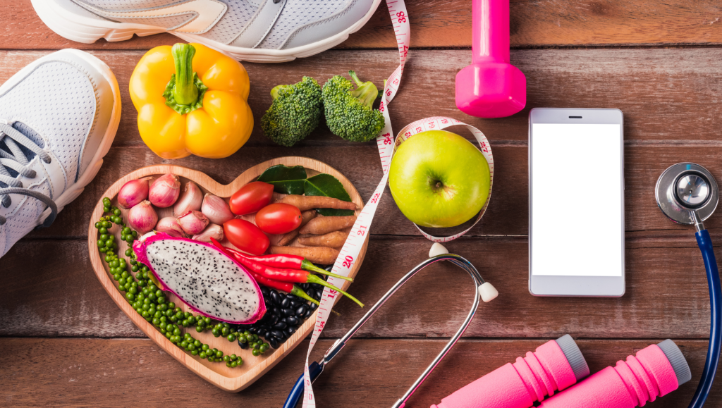 Top view of fresh organic fruit and vegetable in heart plate, shoes, sports equipment and doctor stethoscope, studio shot on wooden gym table. Healthy diet vegetarian food concept. World food day
