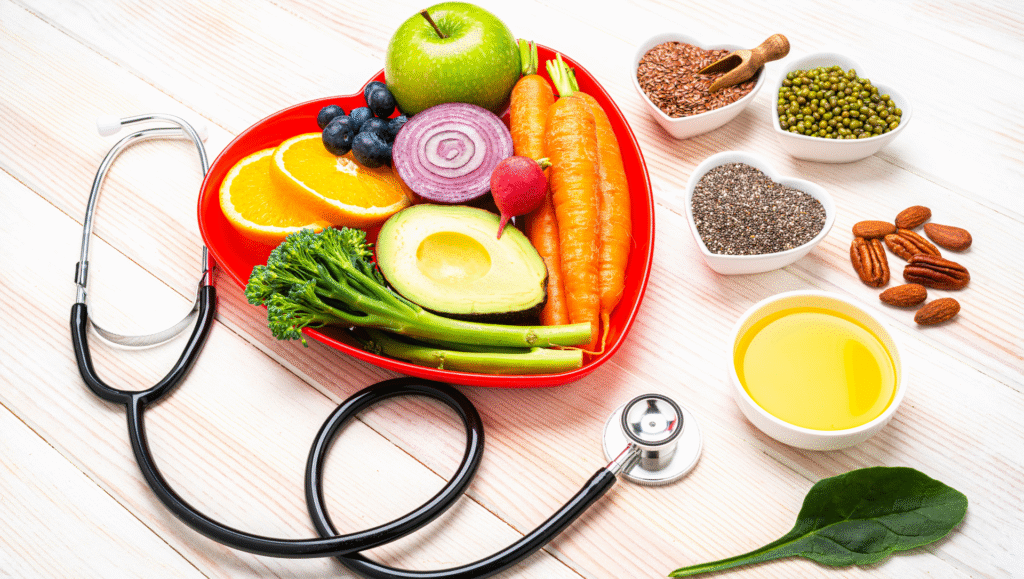 Heart-shaped plate with healthy fruits and vegetables surrounded by seeds, nuts, olive oil, and a stethoscope on a light wooden background.
