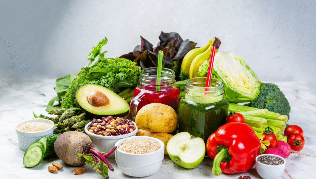 Plant-based foods and green juice surrounded by fresh produce like avocado, beans, peppers, and leafy greens on a white background.