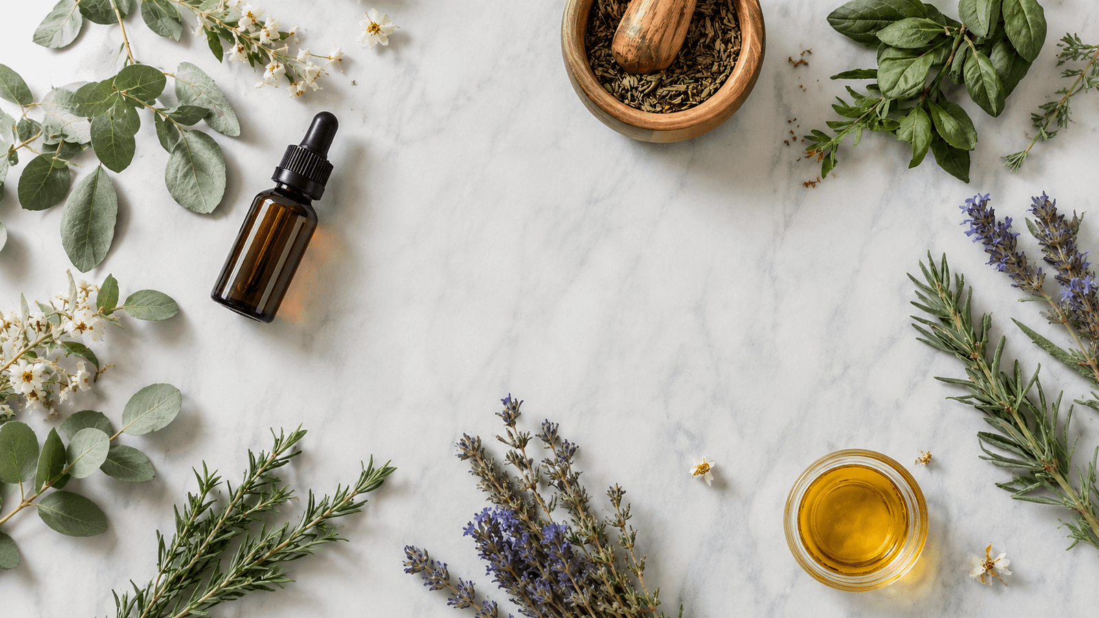 A flat lay view of assorted herbs, dried lavender, and small glass bottles with droppers arranged on a white marble surface.