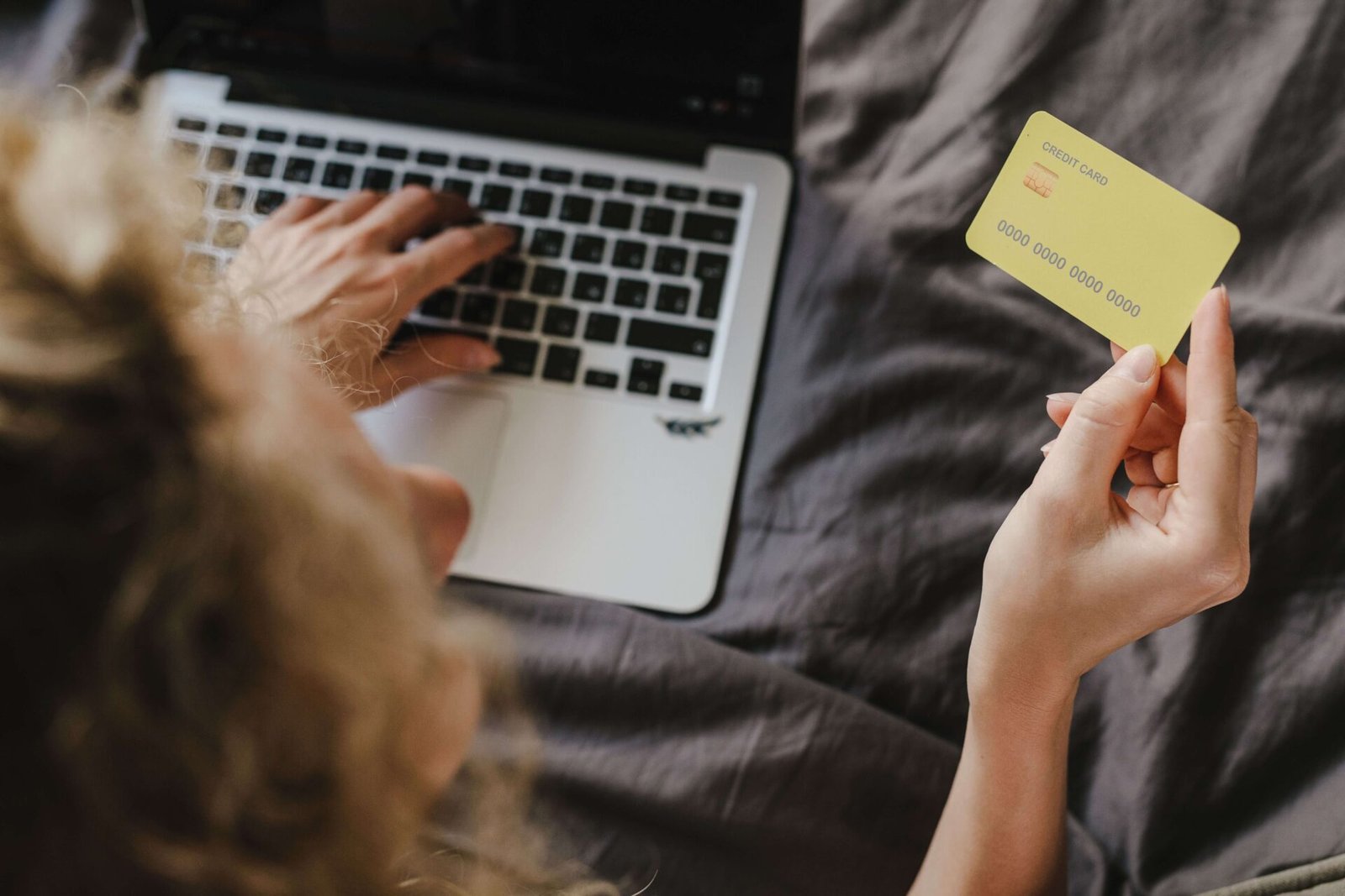 Over-the-shoulder view of a person using a laptop while holding a yellow credit card to make an online purchase