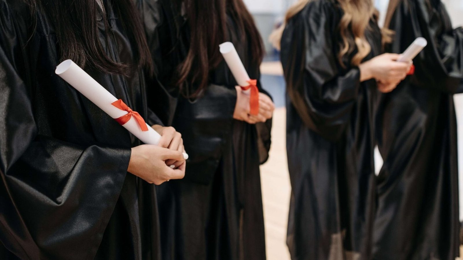 Several graduates wearing black graduation gowns, holding rolled diplomas tied with red ribbons.